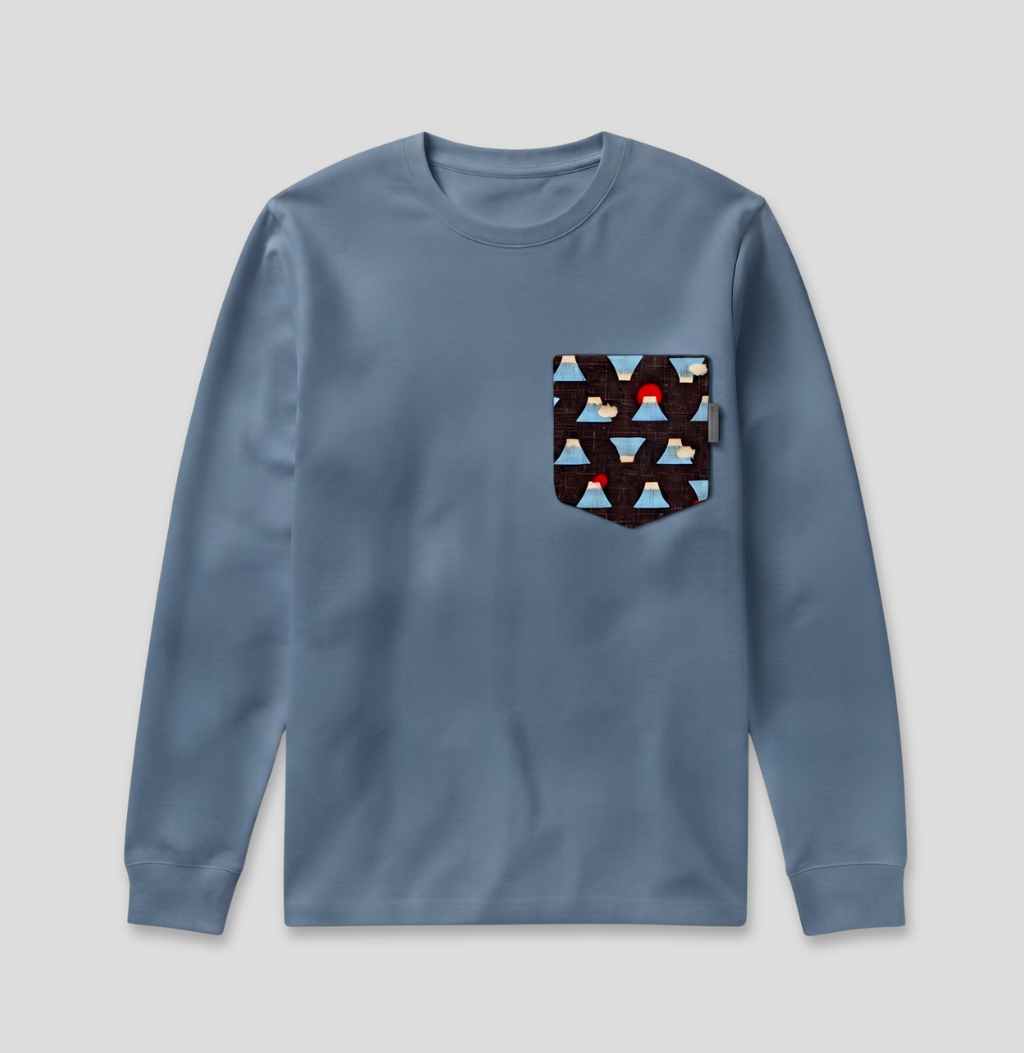 A dusty blue long-sleeve crewneck shirt with a patterned chest pocket featuring triangles in red, brown, and light blue, displayed on a neutral gray background.