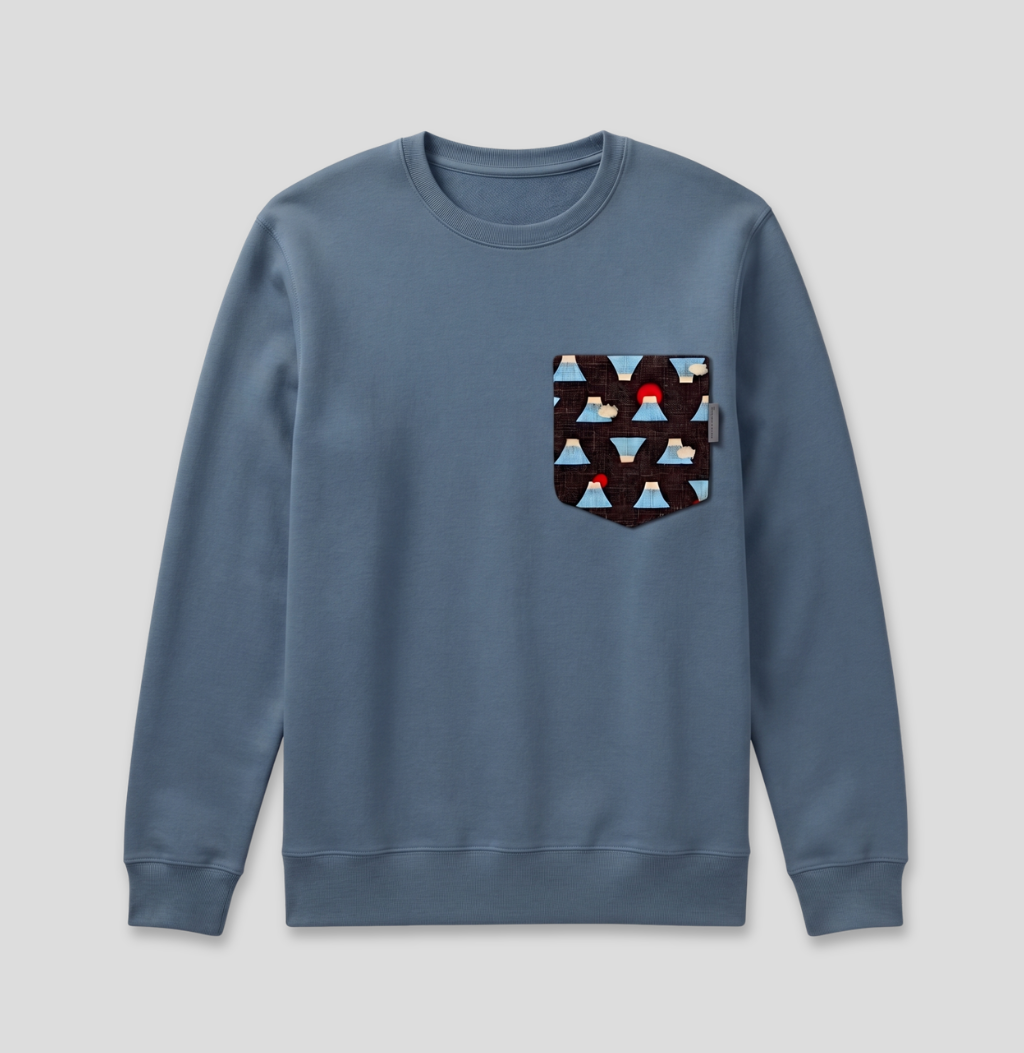 A dusty blue crewneck sweatshirt with a patterned chest pocket featuring triangles in light blue, brown, and white with a small red accent, shown on a light gray background.