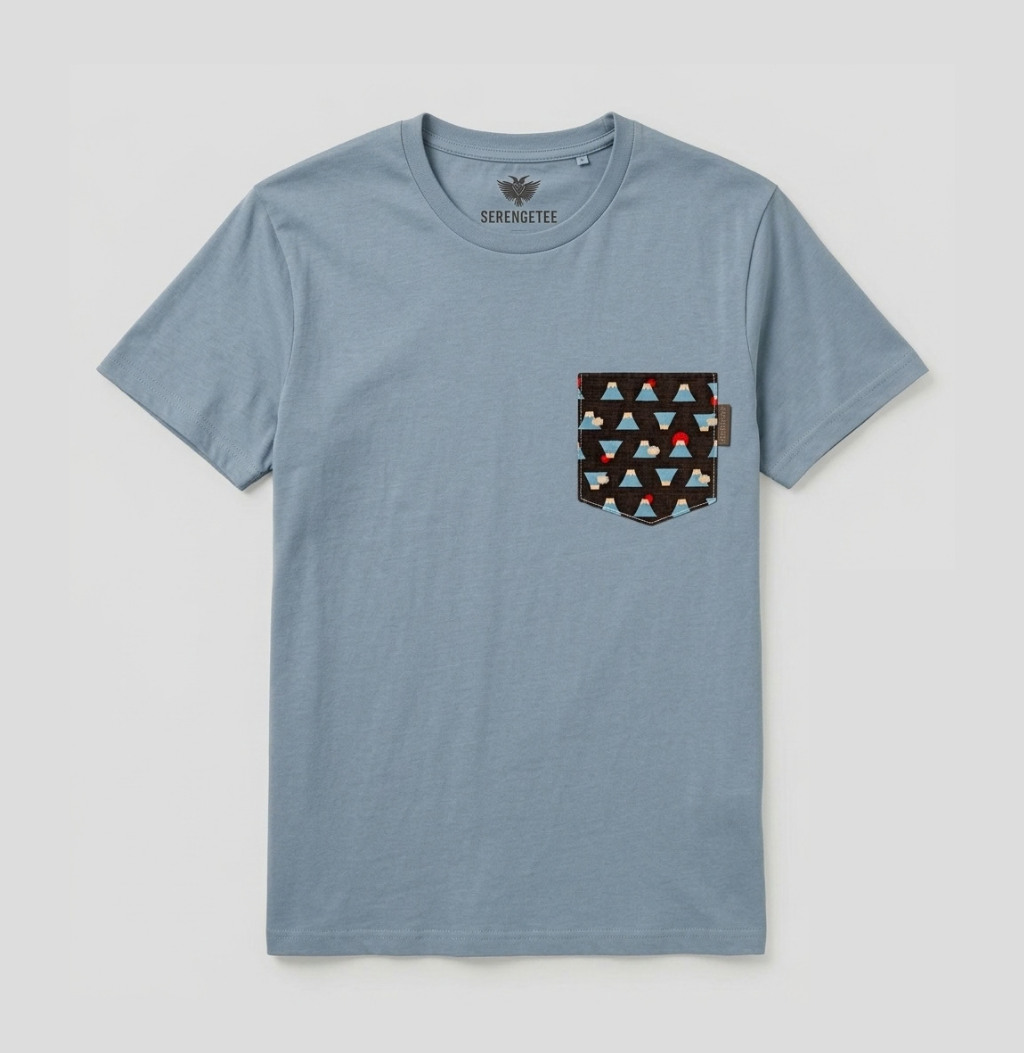 A light blue crewneck t-shirt by Seremete, featuring a geometric patterned chest pocket with red, black, and white triangles, displayed flat against a light gray background.