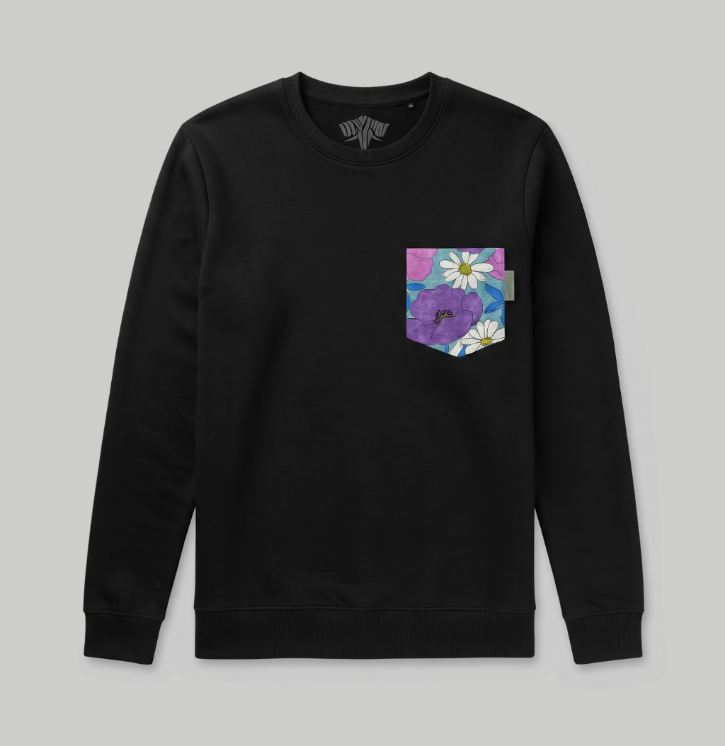 A black crewneck sweatshirt with a floral pocket on the left chest, featuring purple flowers and white daisies on a pink and blue background, shown against a solid gray backdrop.