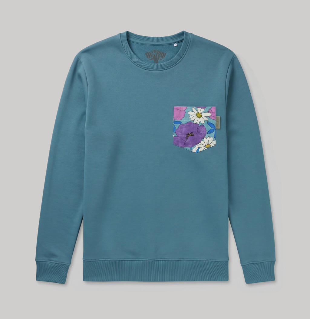 A teal blue crewneck sweatshirt with a floral chest pocket featuring purple flowers and white daisies, shown flat on a light gray background.
