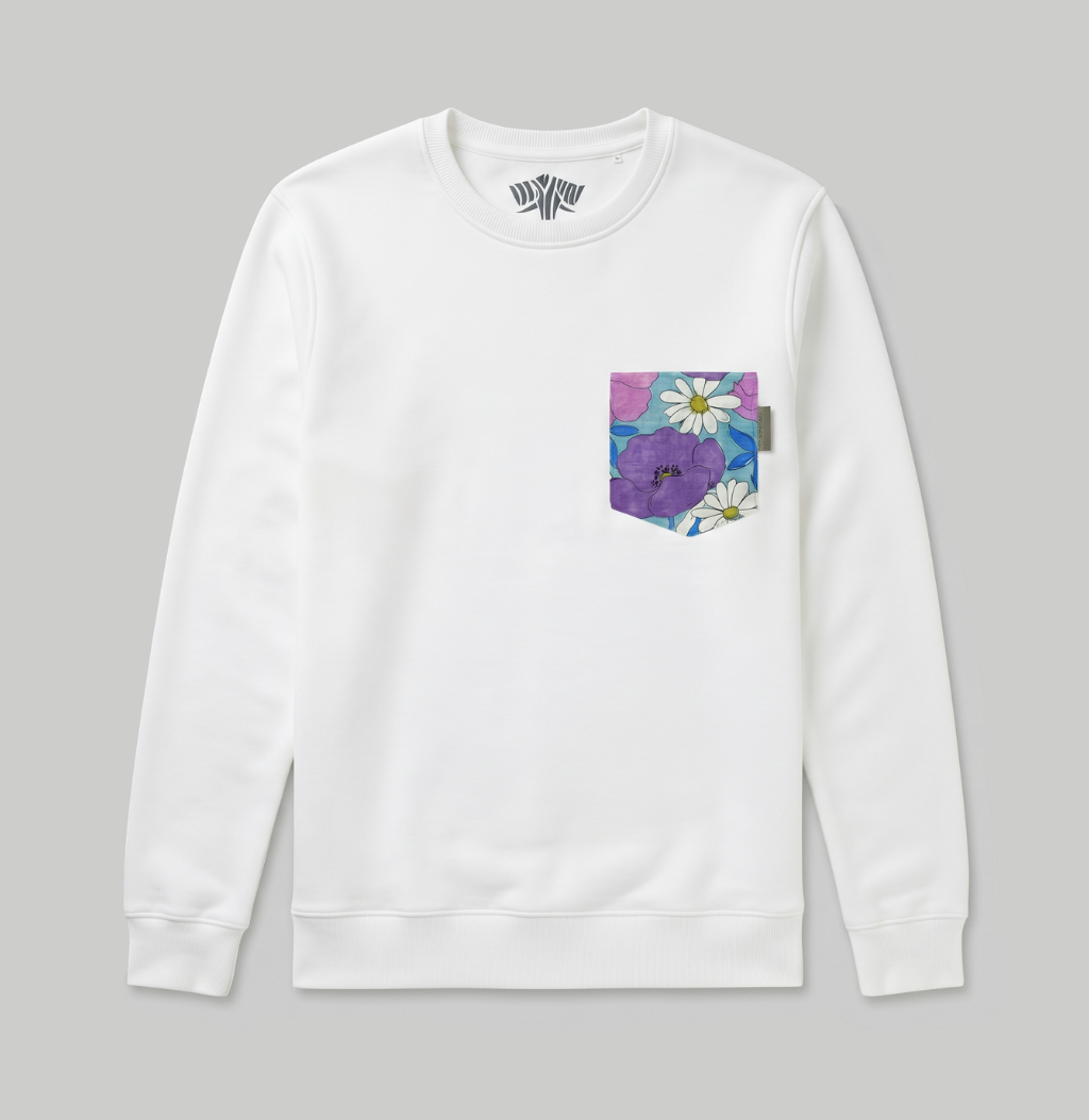 A white crewneck sweatshirt with a small floral chest pocket on the left side, featuring purple flowers and white daisies on a blue and pink background, shown against a solid gray backdrop.