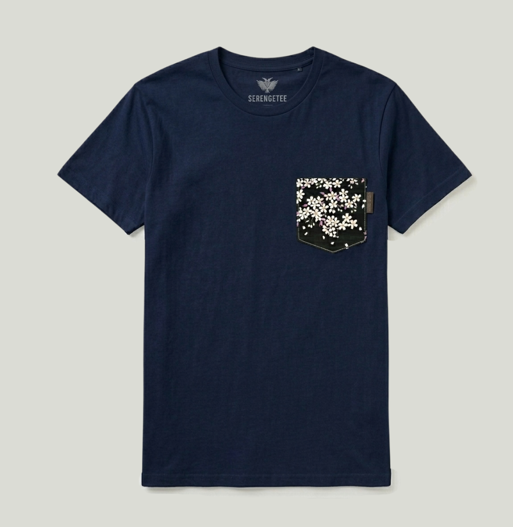 A navy blue short-sleeve crewneck t-shirt by Serenitee, featuring a chest pocket decorated with a black and white cherry blossom pattern, shown against a light gray background.